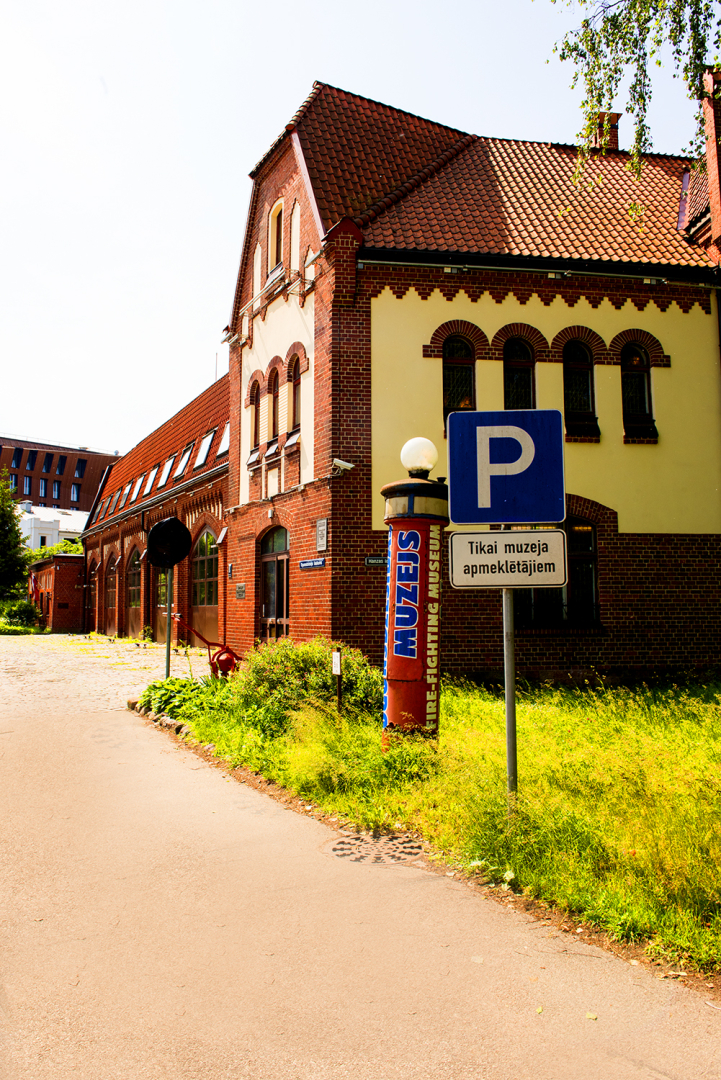 Muzeja ēka Hanzas ielā 5 no Hanzas ielas puses, priekšplānā autotransporta stāvvietu apzīmējošā ceļa zīme